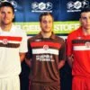 Die Spieler vom FC St. Pauli BRUNS, LEHMANN und DAUBE (vlnr) präsentieren die neuen Trikots. Das rote Trikot ist das Torwarttrikot und wird im DFB Pokal eingesetzt.